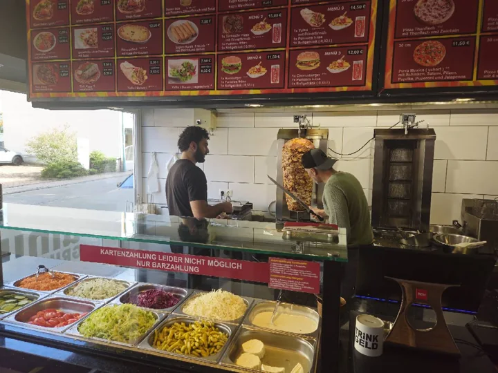 Mitarbeiter schneiden Dönerfleisch am Spieß hinter der Theke im Umut Grillhaus